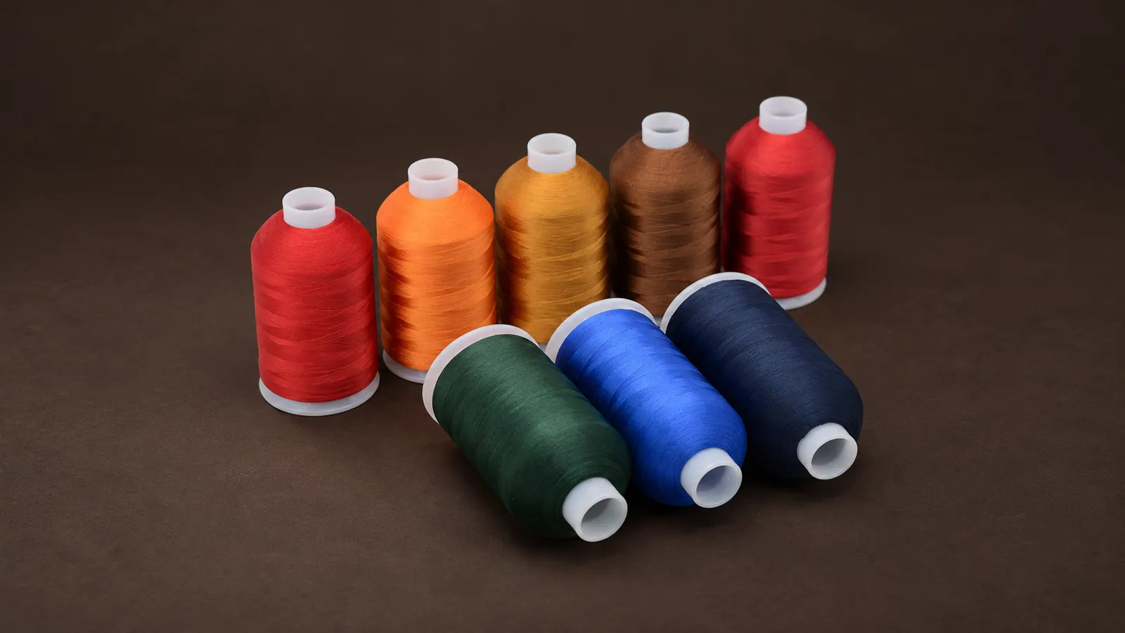 Polyester Embroidery Thread. Eight compact thread cones in warm and cool colors with white cores. Source-based AI-edited visualization.